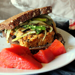 A tempeh sandwich on a white plate with red garnish