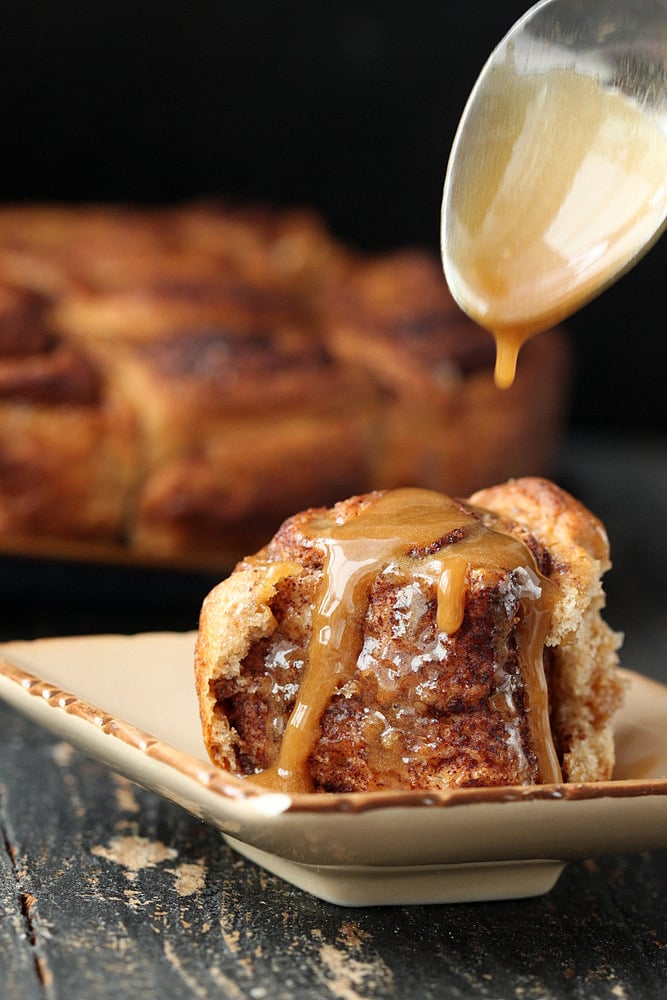 vegan cinnamon rolls maple coffee icing being drizzled on top of vegan cinnamon rolls