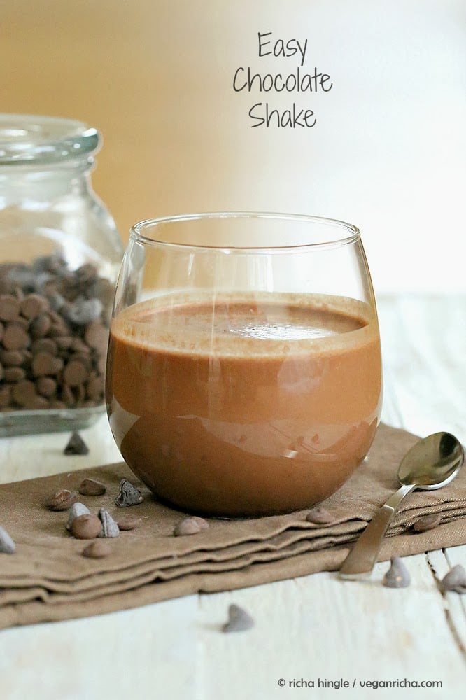 side view of a healthy vegan chocolate milkshake with a mason jar with chocolate chips in the background