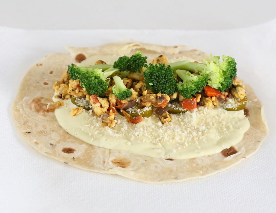 tempeh scramble a wrap topped with cashew cream, tempeh scramble and veggies ready to be rolled