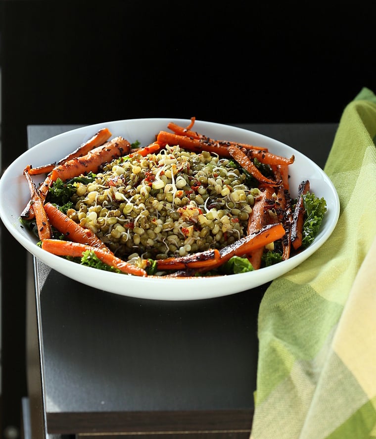 kale salad recipe side view of a bowl of kale salad topped with sprouted mung beans and seared carrots