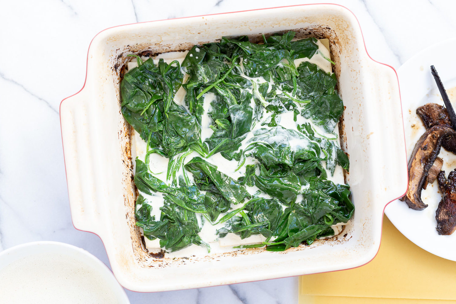 Lasagna noodles layered with spinach and garlic sauce for Our Creamy Vegan Mushroom Lasagna