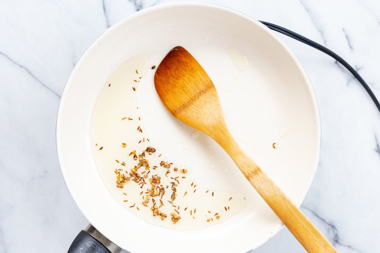 Spices in oil in a white skillet