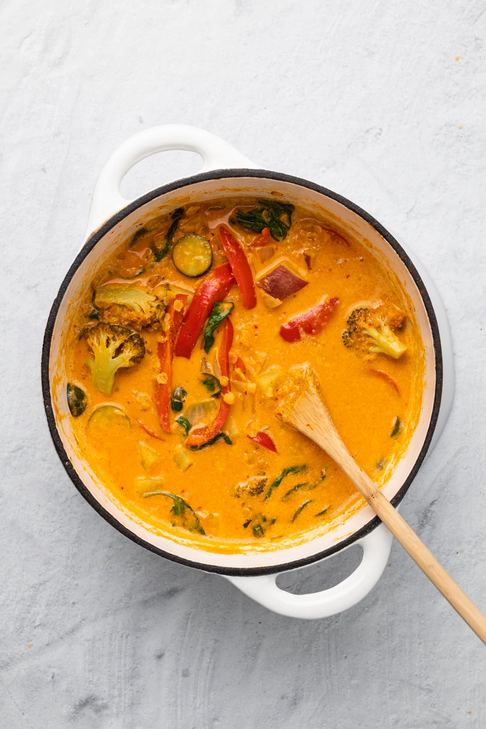 sweet potato curry overhead shot of a pot of vegan red lentil sweet potato curry in a white pot with a wooden spoon