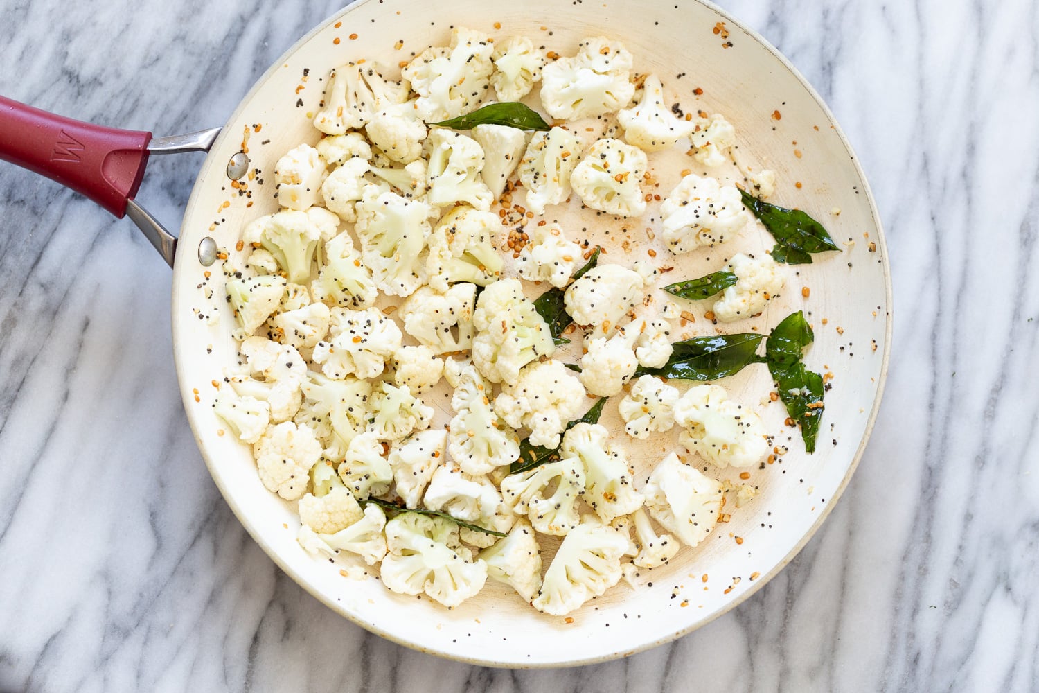 raw cauliflower florets being added to frying pan with Indian spices
