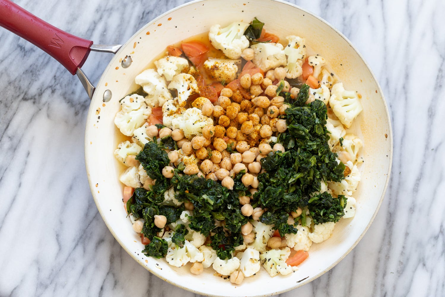 chickpeas and spinach being added to spices and par-cooked cauliflower to make Indian chickpea saute