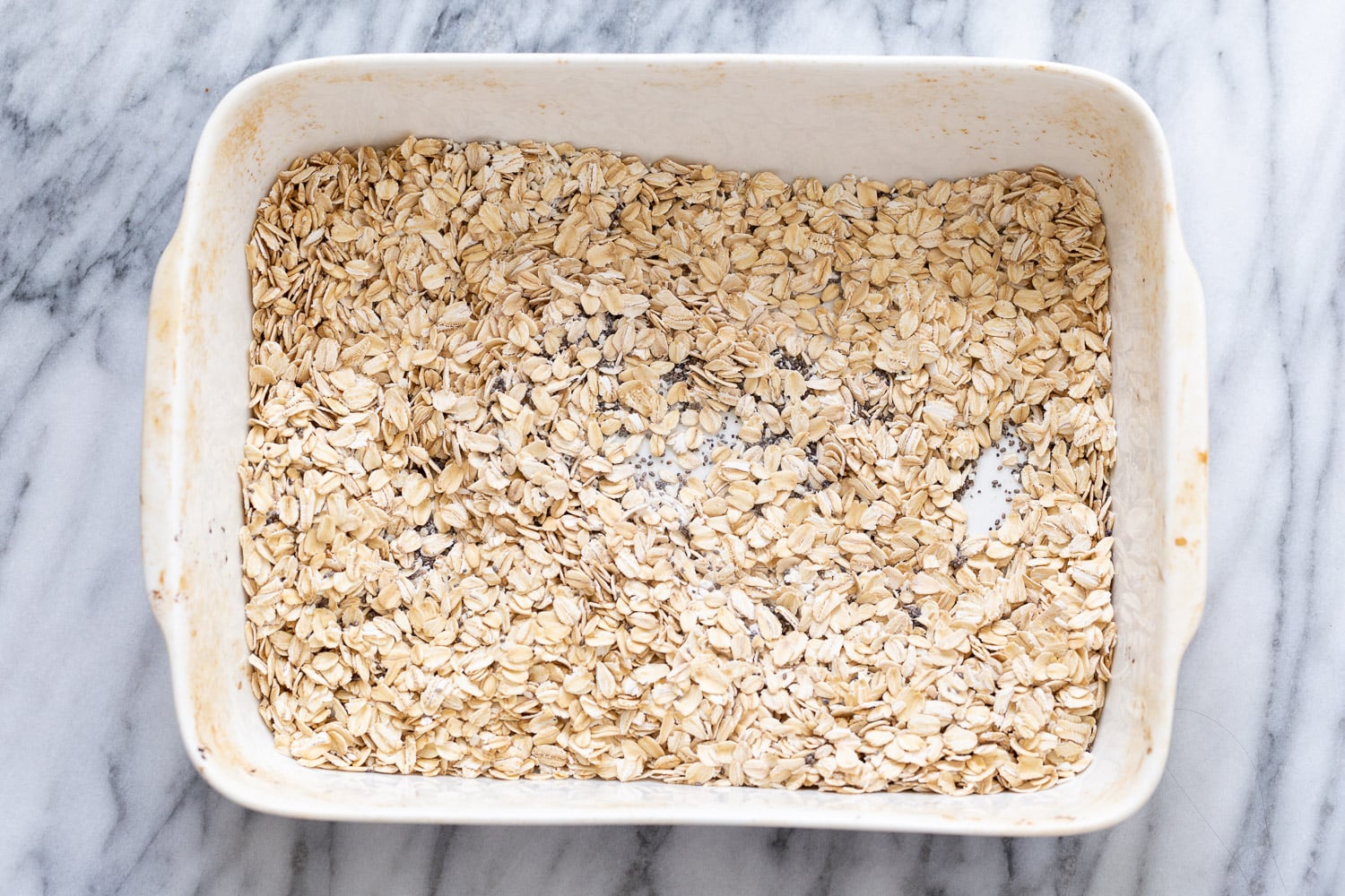 vegan baked oatmeal overhead shot of a casserole dish filled with rolled oats and chia seeds