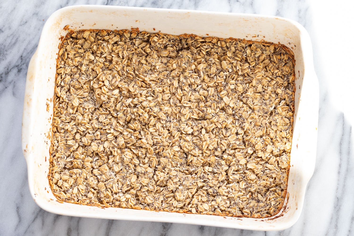 vegan baked oatmeal overhead shot of freshly baked vegan baked poppyseed and lemon oatmeal in a white casserole dish