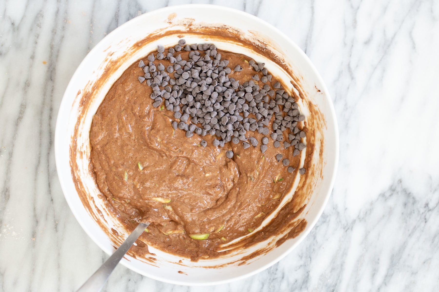 overhead shot of a white bowl with vegan zucchini bread batter sprinkled with chocolate chips 
