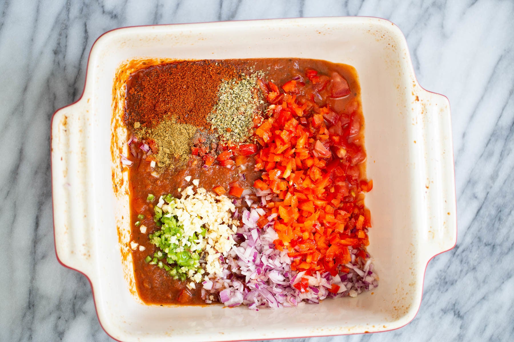 chili mix being tossed in a white casserole dish 