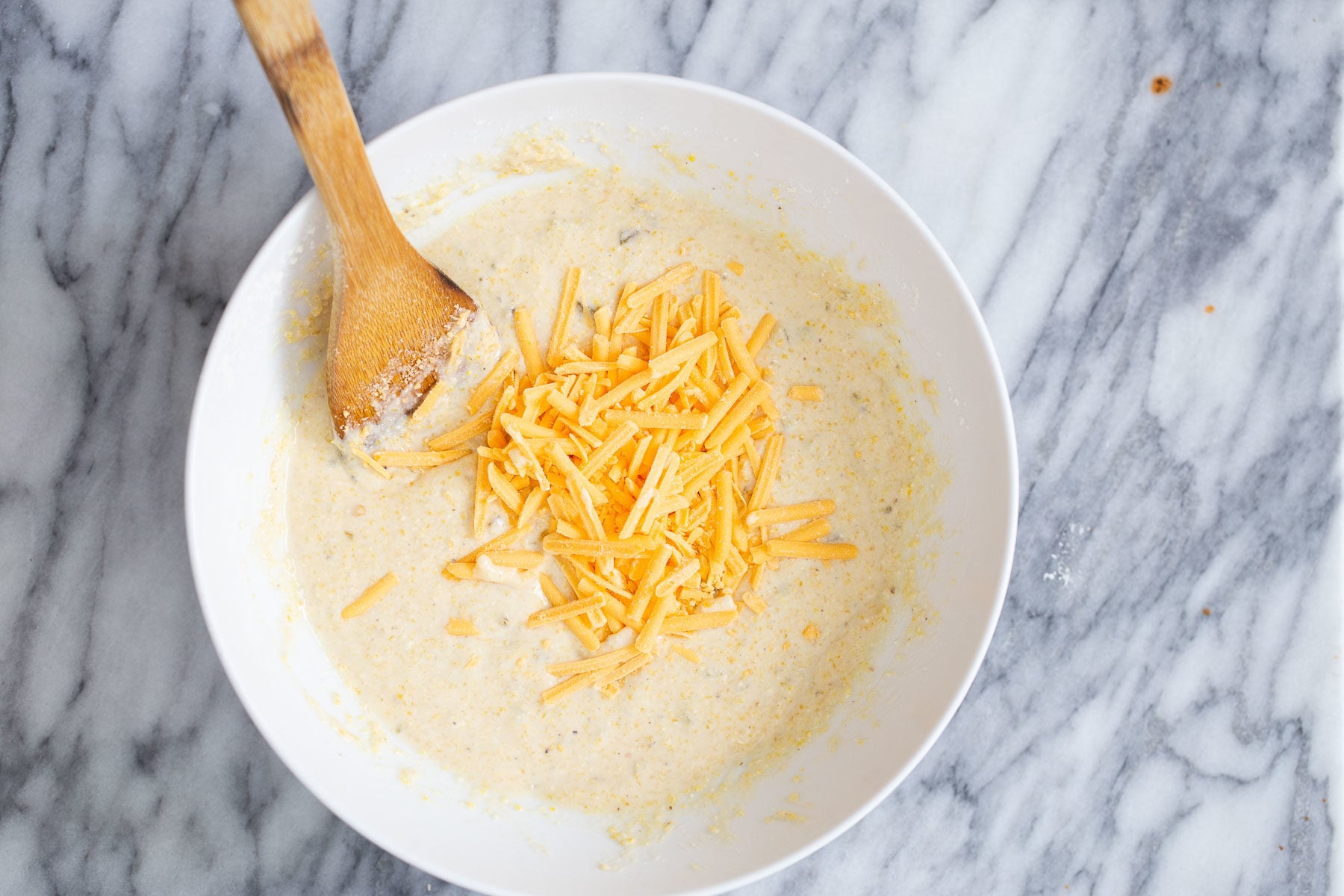 cheddar shreds being stirred into cornbread batter
