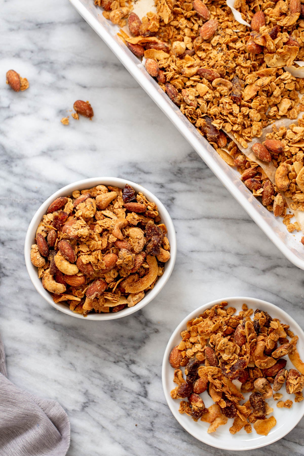coconut granola two small bowls of homemade baked vegan almond coconut granola next to a baking sheet with granola