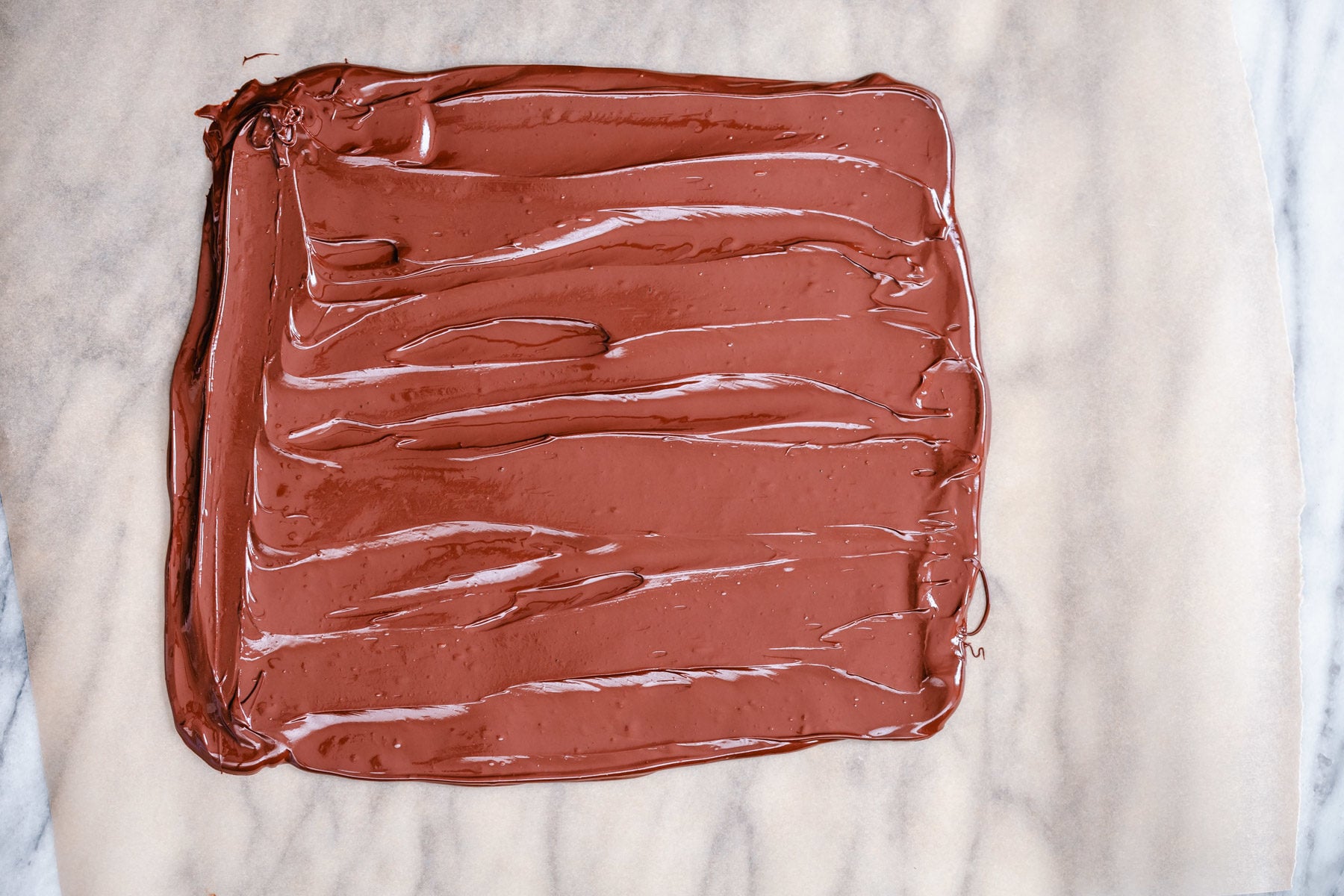 peanut butter chocolate bark melted chocolate being spread out into a rectangle to make chocolate bark