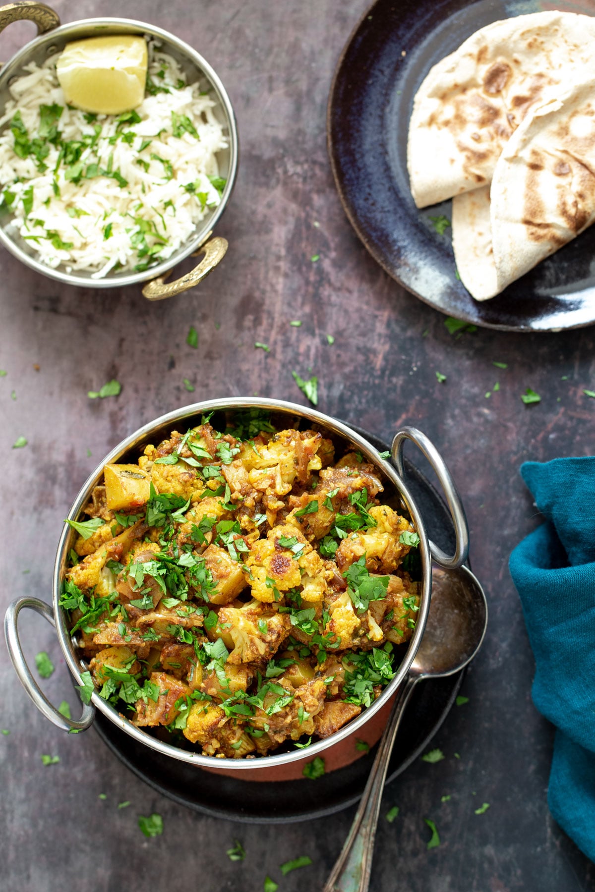a bowl of vegan aloo gobi next to a small dish with rice and some flatbread