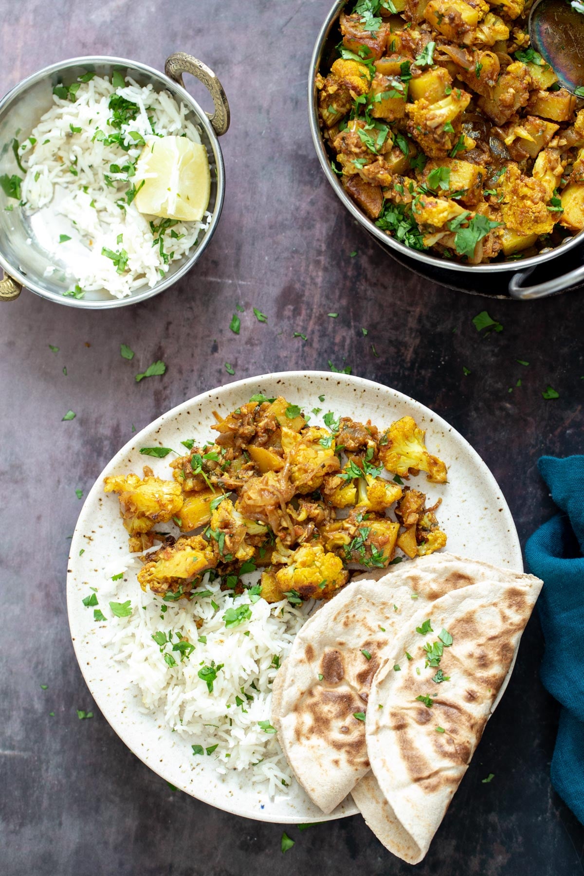 a plate with a serving of aloo gobi, rice and 2 folded naan breads