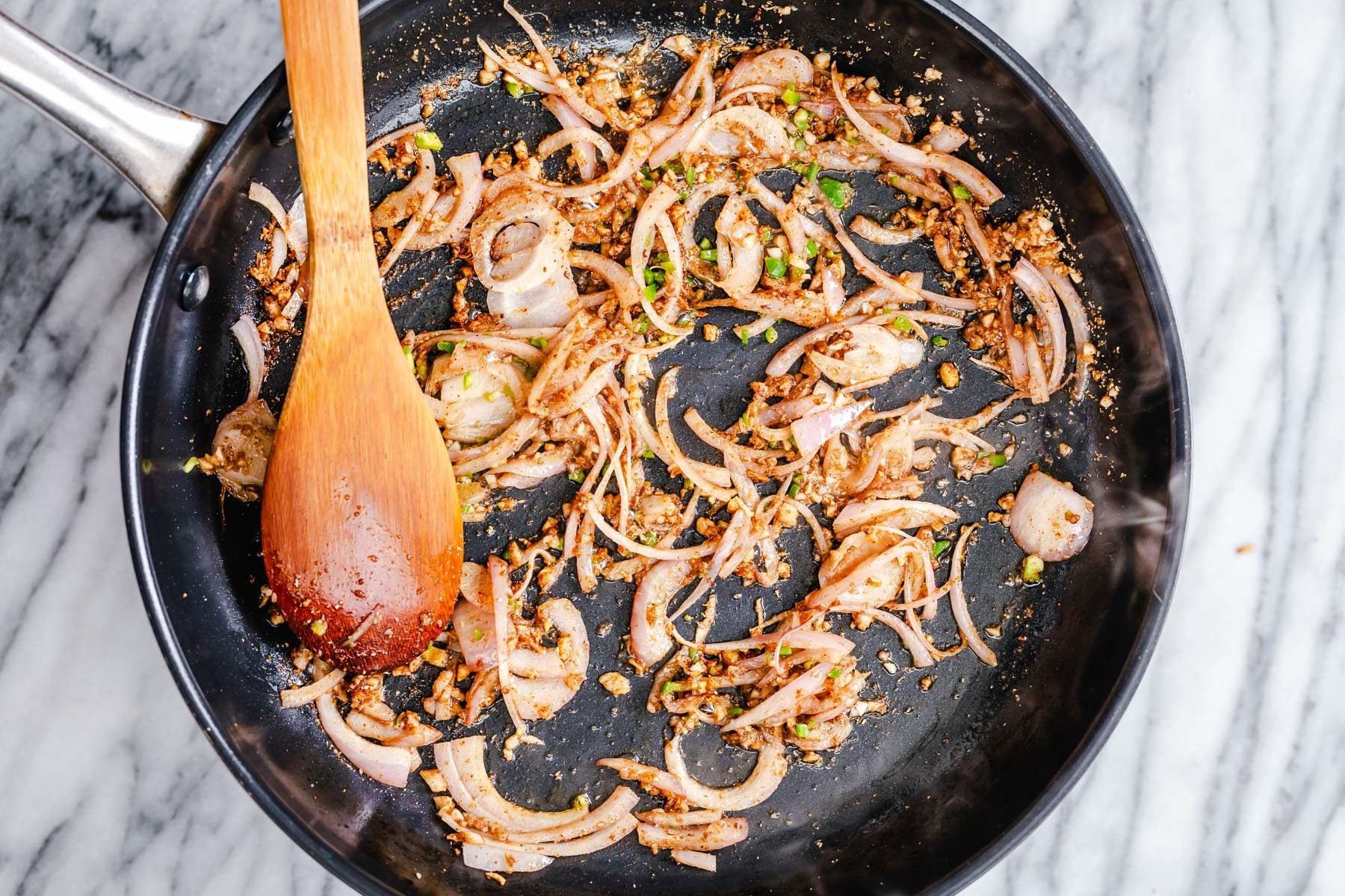 onion ginger and garlic being sauteed with spices in a large frying pan