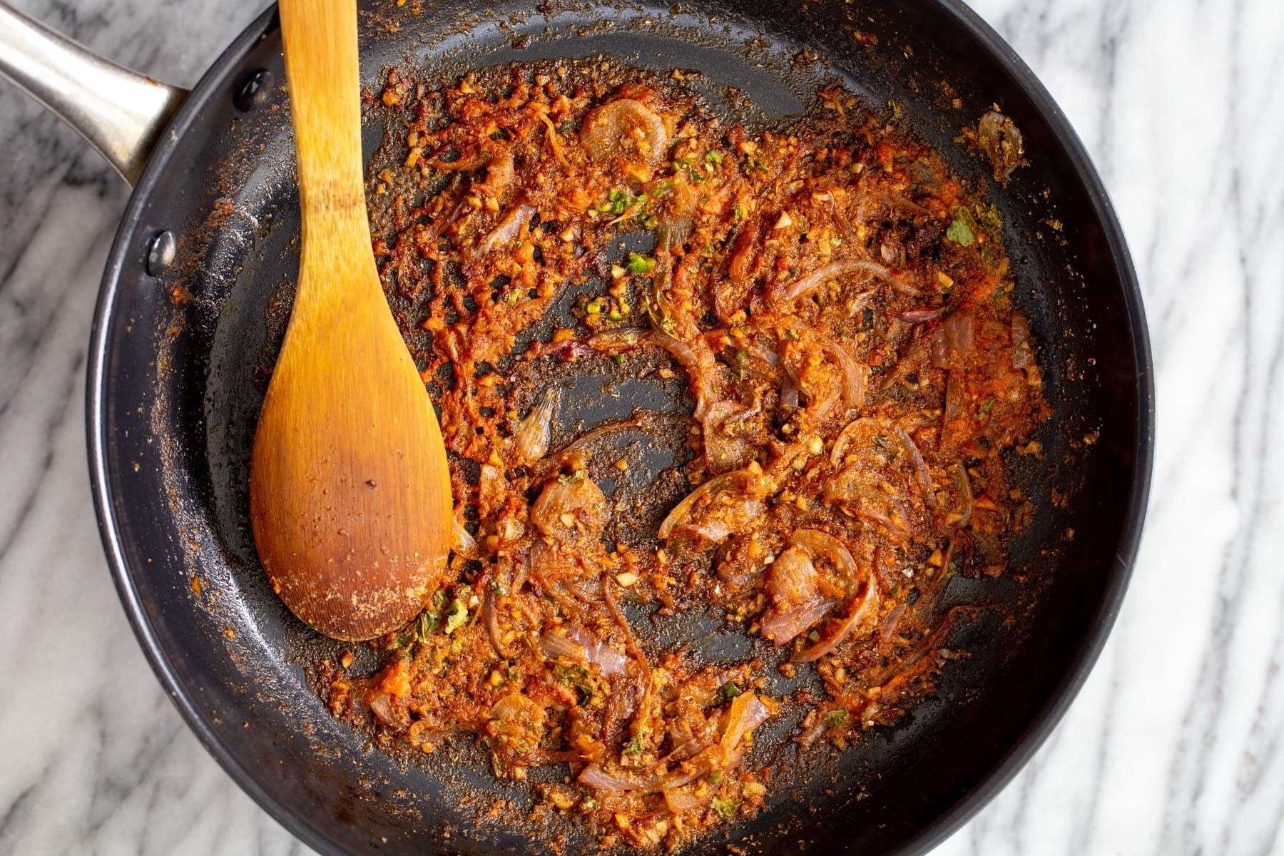 onion and garlic being sauteed with spices and tomato puree in a black frying pan 