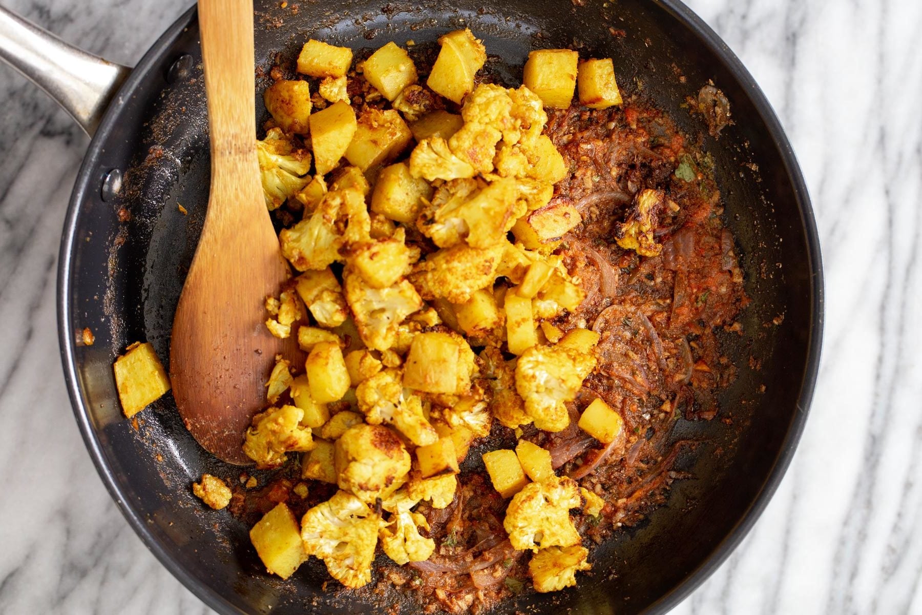 cauliflower and potato cubes being tossed with sauteed spices 
