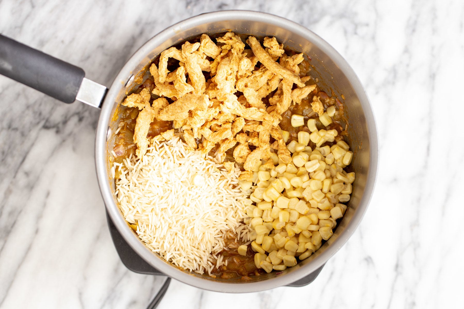 vegan enchilada soup rice, soy chunks and corn being added to a pot with vegan enchilada soup