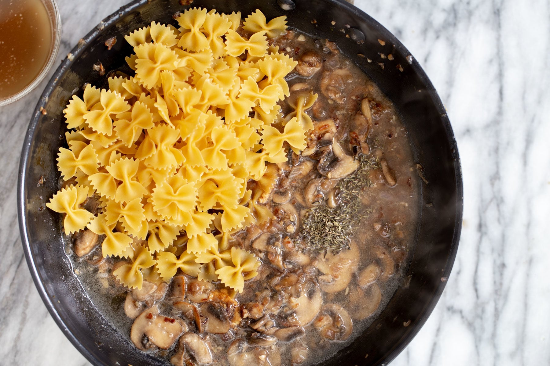 farfalle pasta being added to a pan with mushroom sauce