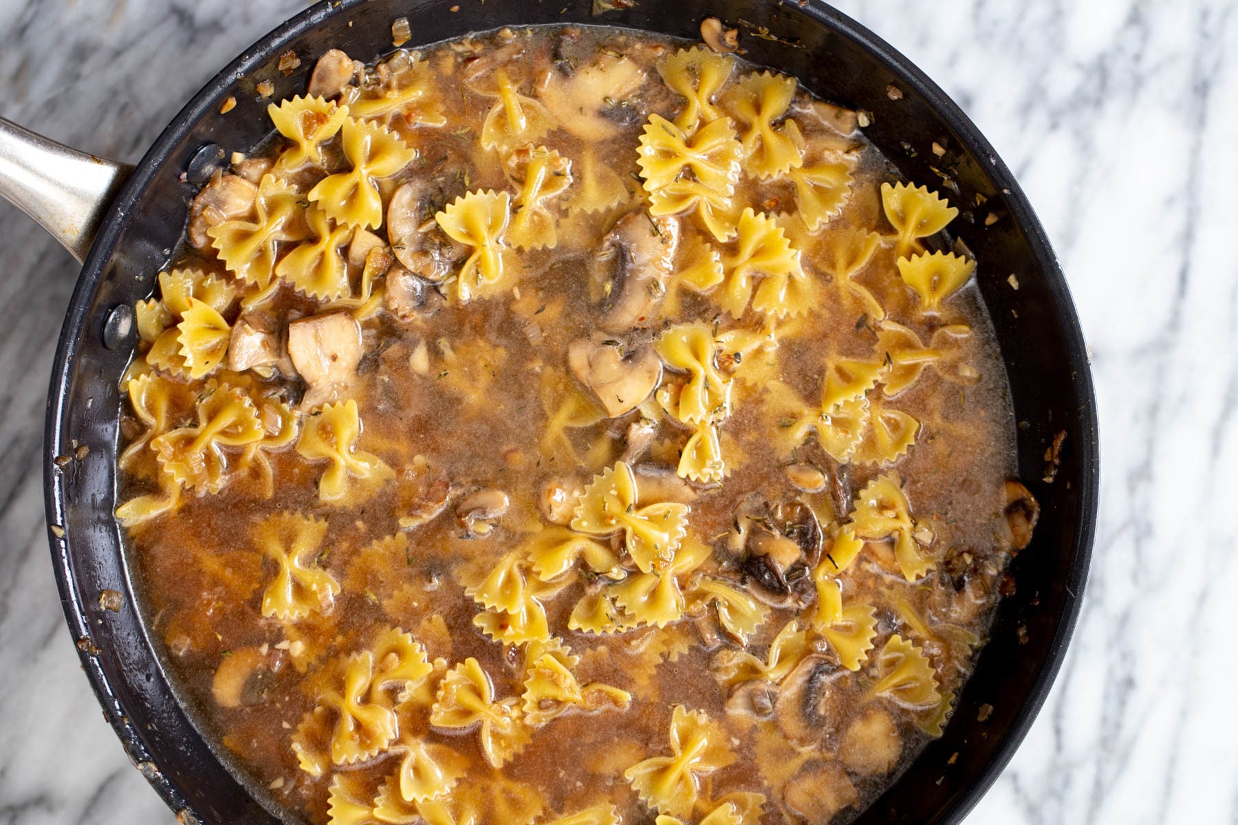 uncooked farafalle pasta and mushroom sauce cooking in a saucepan