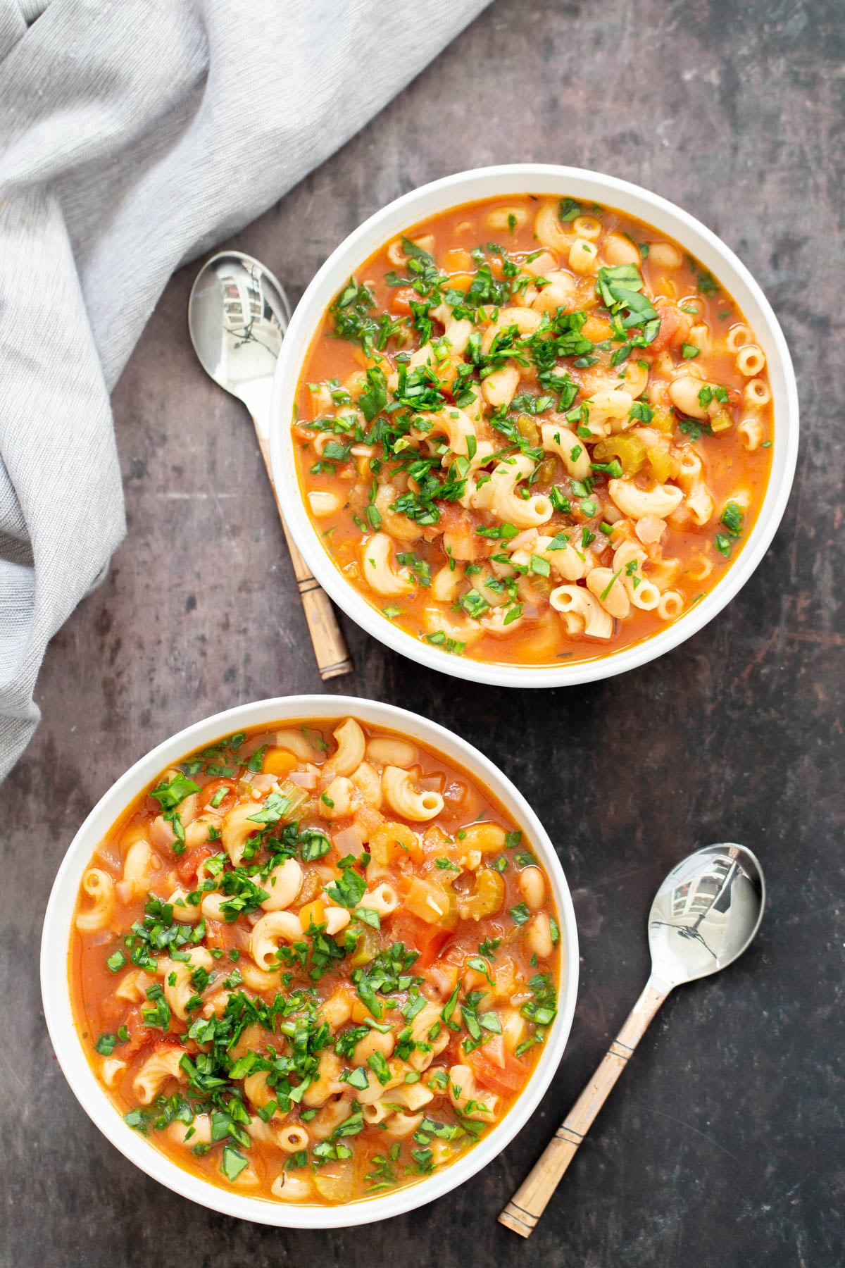 overhead shot of two bowls of vegan pasta e fagioli garnished with chopped basil 