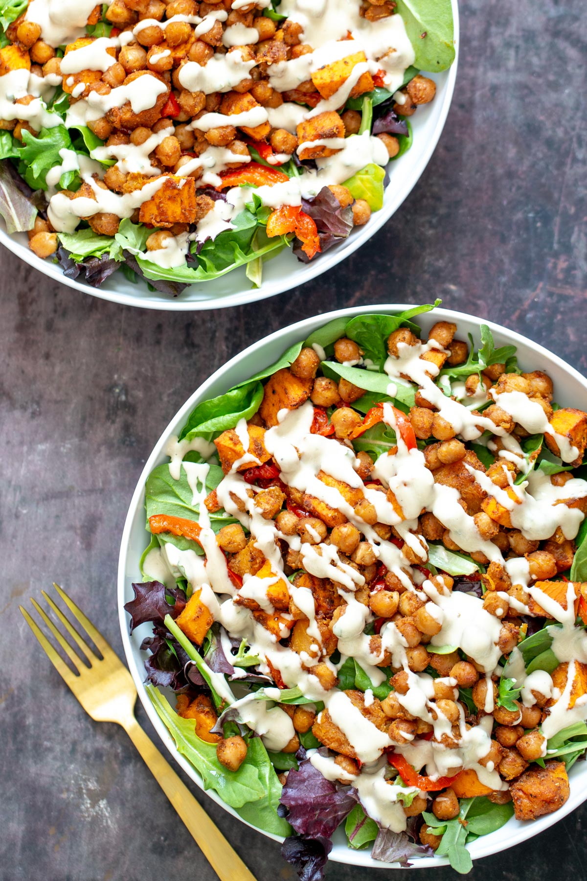 sweet potato salad two bowl with leafy greens topped with roasted chickpeas and cubed sweet potato