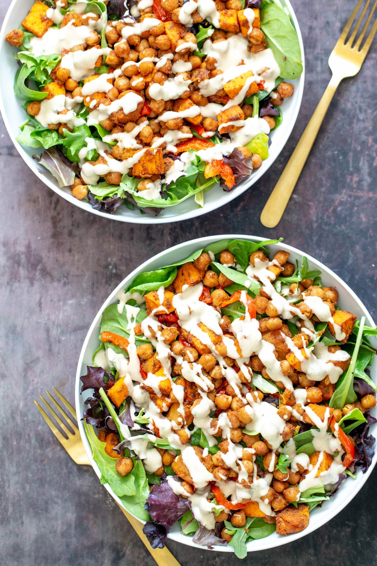 two bowls of vegan baked chickpea sweet potato salad bowls drizzled with tahini dressing 