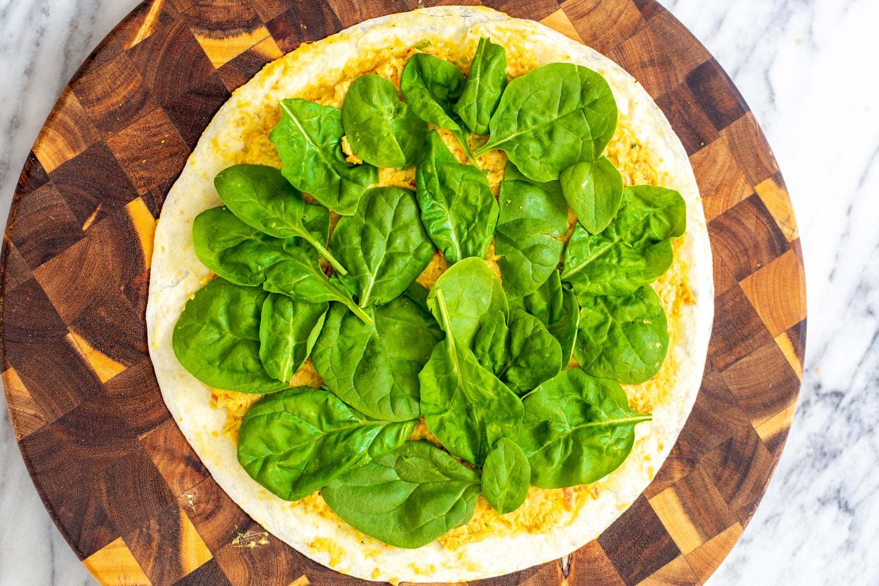 chickpea breakfast tortilla topped with chickpea scramble and fresh spinach on a wooden board