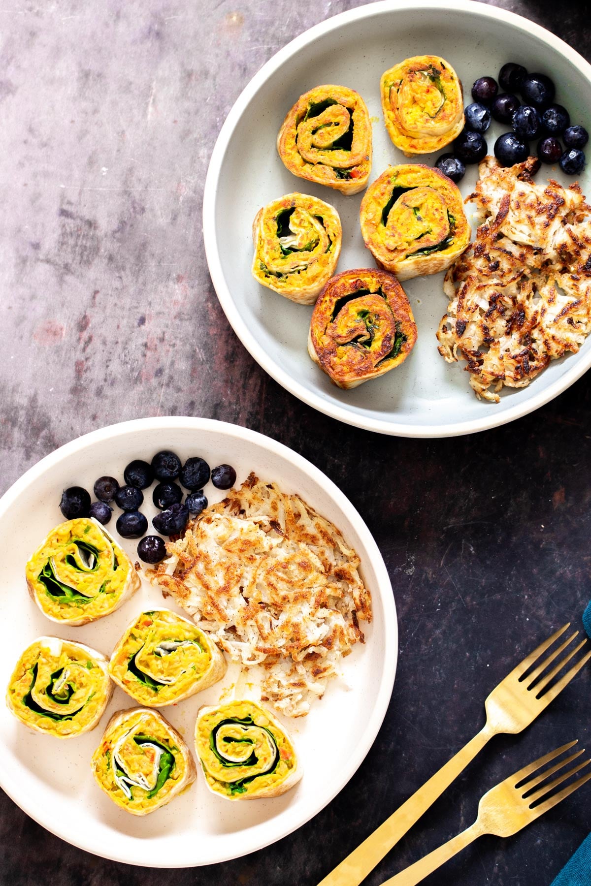 chickpea breakfast two plates with vegan chickpea breakfast scramble pinwheels served with berries and hashbrowns