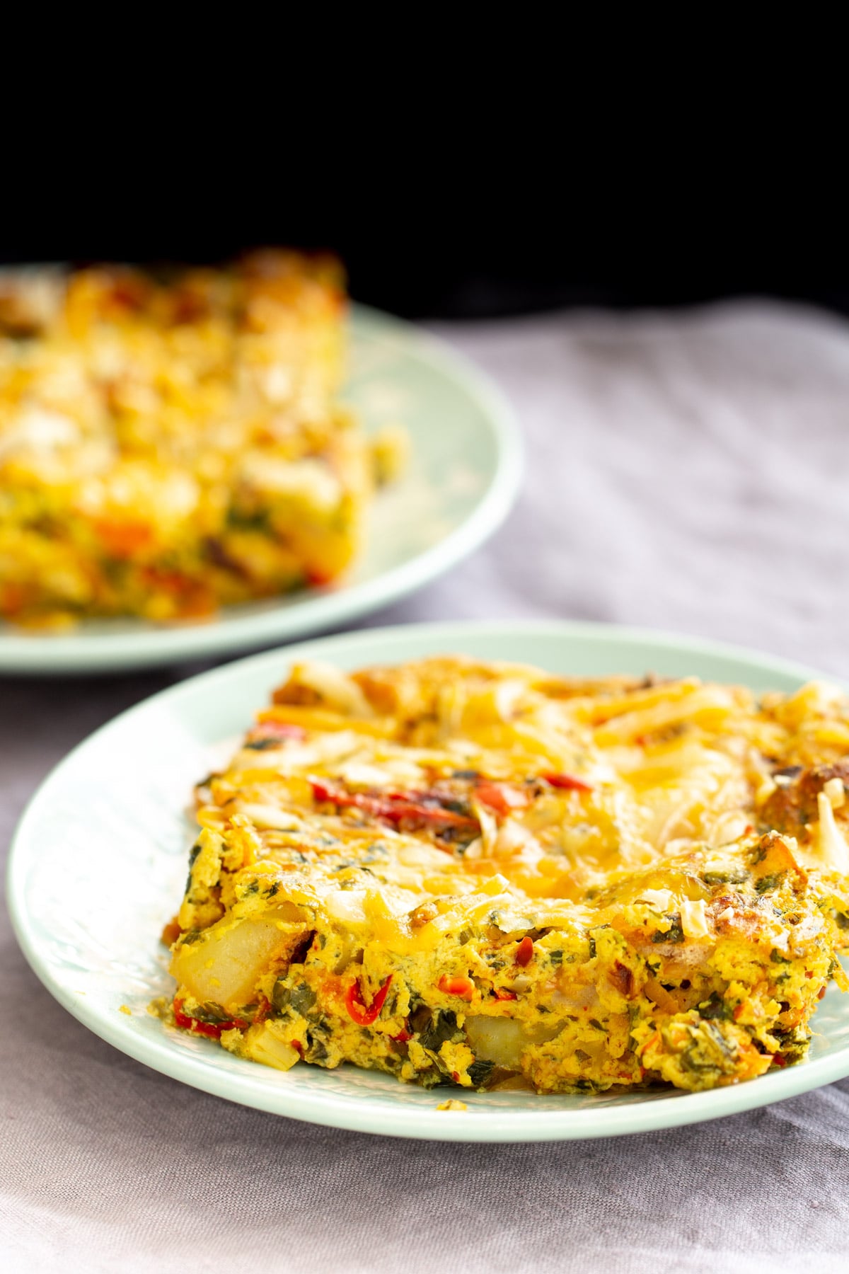two plates with vegan Mexican egg breakfast casserole with bell pepper, potatoes and onions