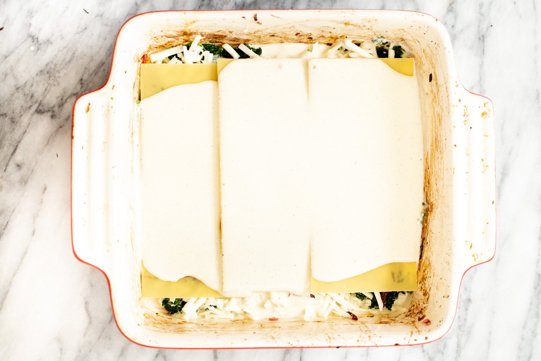 tofu bechamel sauce poured over lasagna sheets in casserole dish to make vegan lasagna recipe