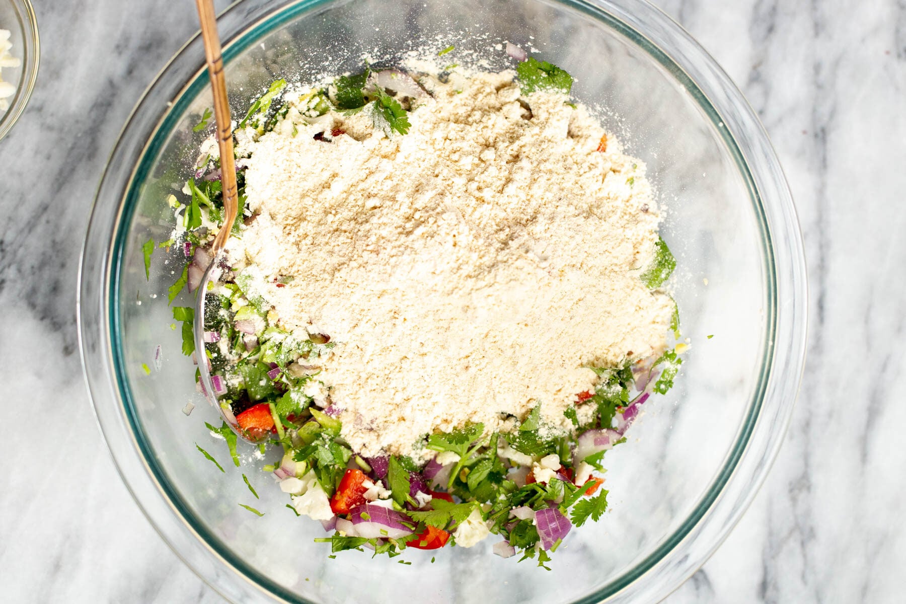 chickpea flour being added to chopped veggies in a bowl