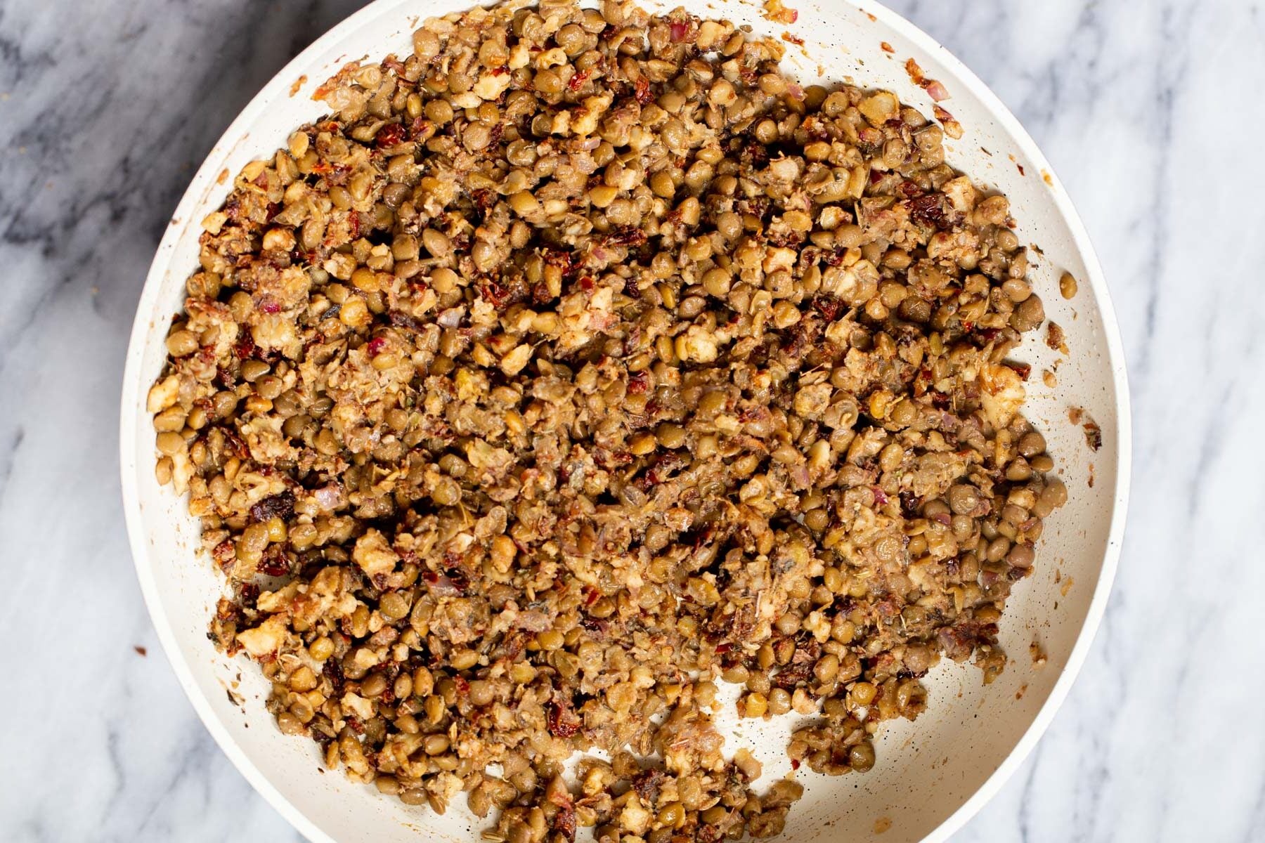 mashed lentils and sauteed onions in a white sauteeing pan