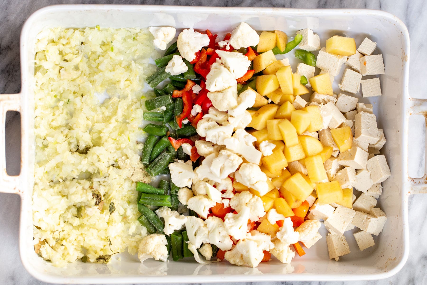 Navratan Korma tofu cubes, veggies and minced ginger and garlic in a white casserole dish