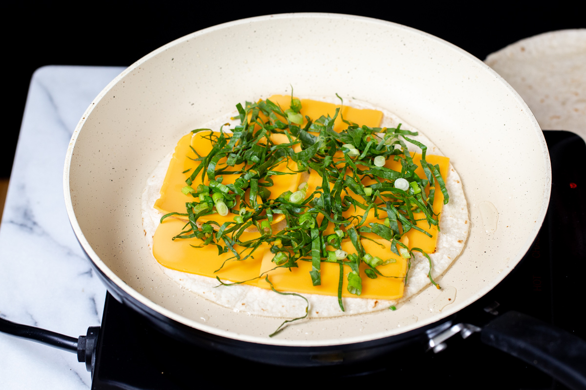 tortilla topped with vegan cheese and chopped greens in a pan