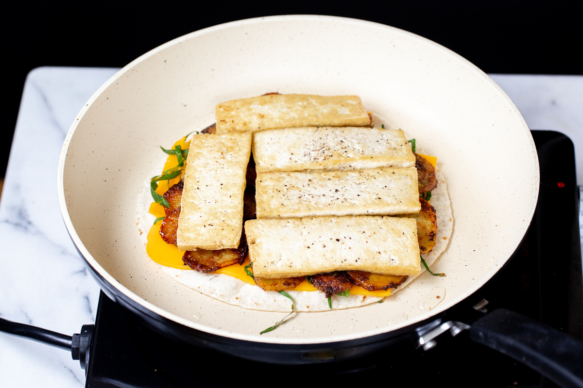 vegan quesadilla being topped with cheese and tofu slices