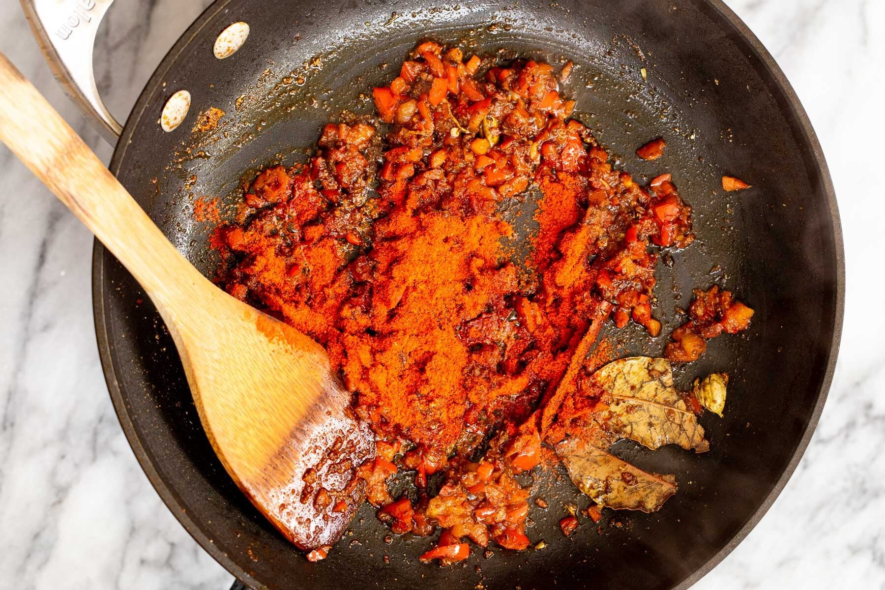ground spices being added to bell pepper and whole spices in a sauteeing pan