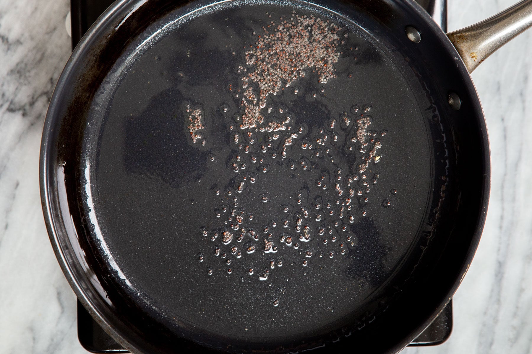 mustard seeds frying in oil in black frying pan