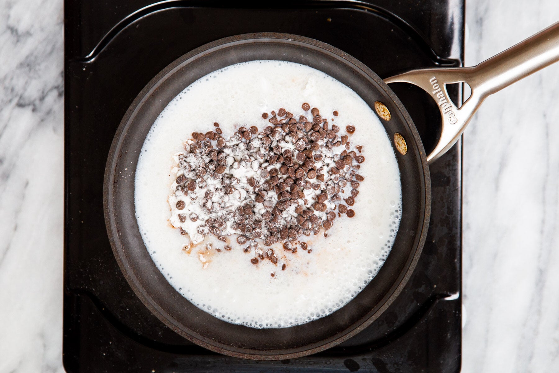 chocolate chips being added to hot coconut milk in a pot 