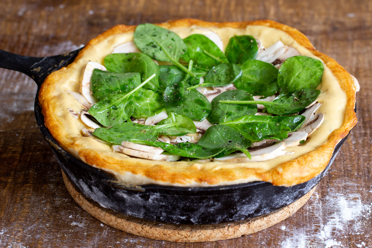 vegan pretzel crust pizza in a black skillet topped with mushrooms and spinach