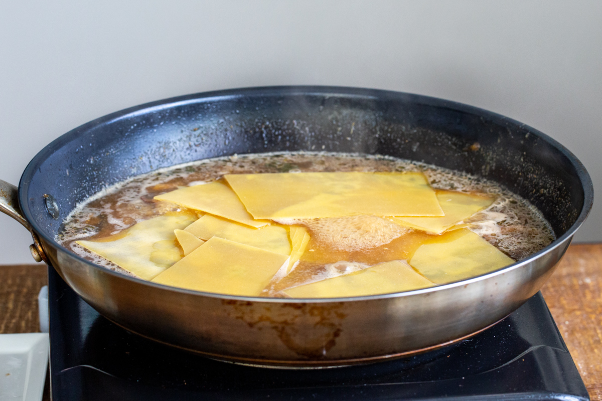 broken lasagna noodles being added to mushroom broth to make skillet lasagna