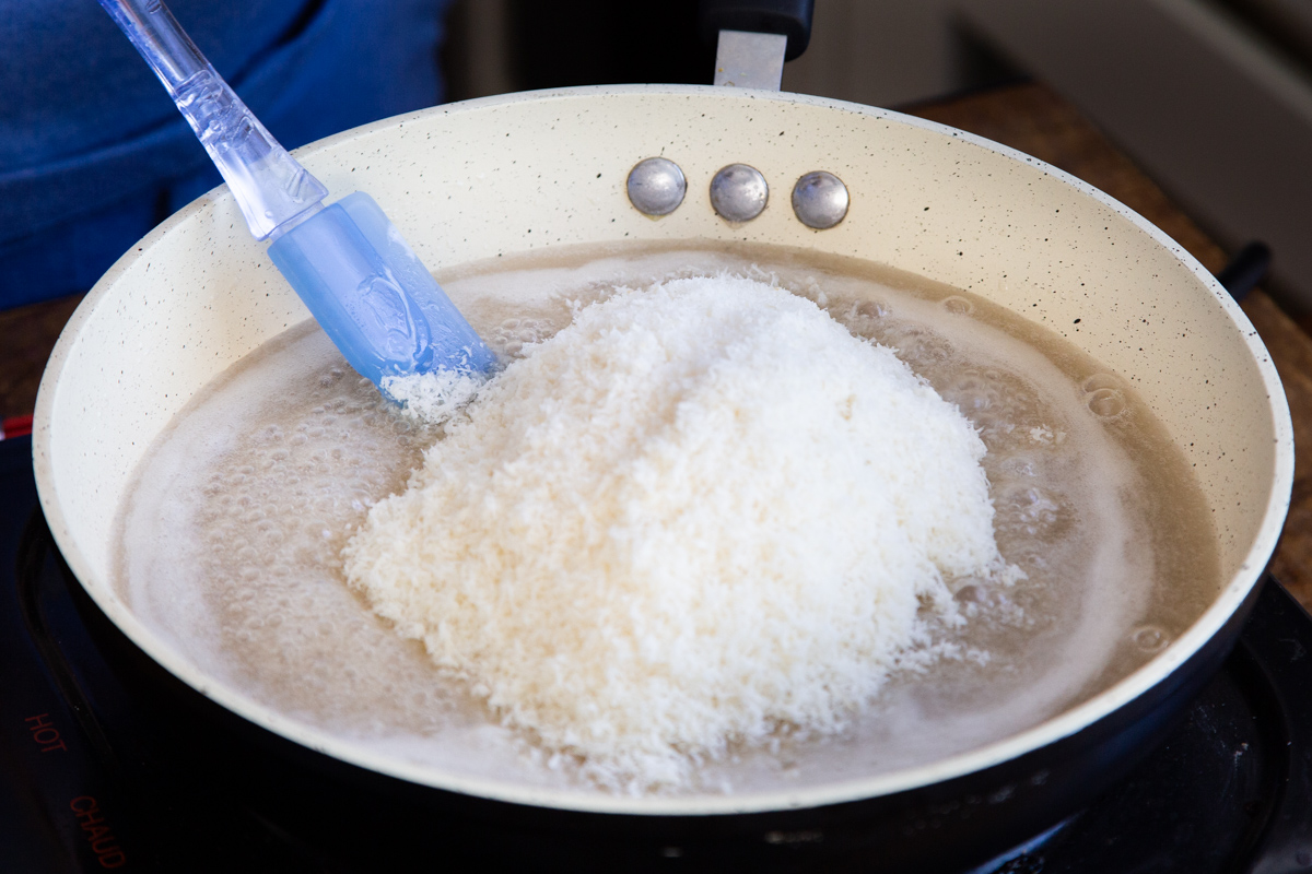 shredded coconut being added to a sauteeing pan with coconut milk