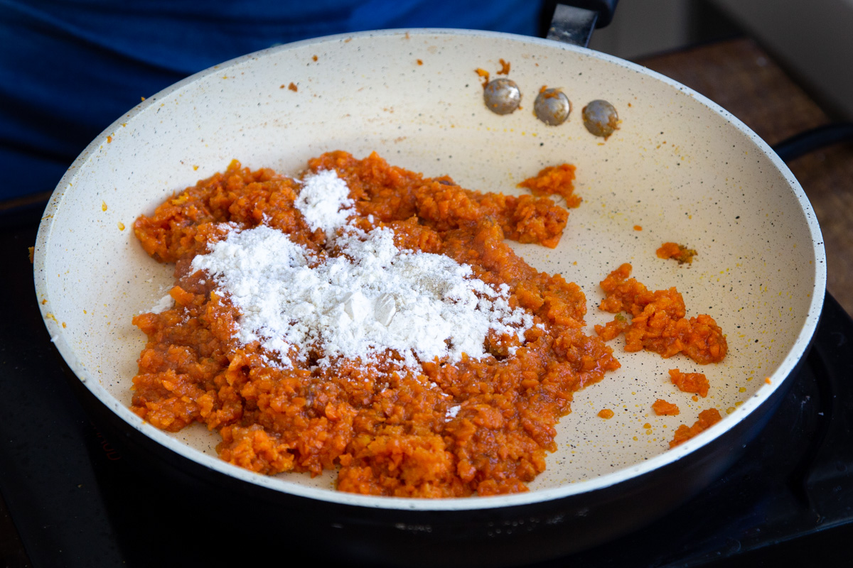 flour being added to shredded carrots in a frying pan