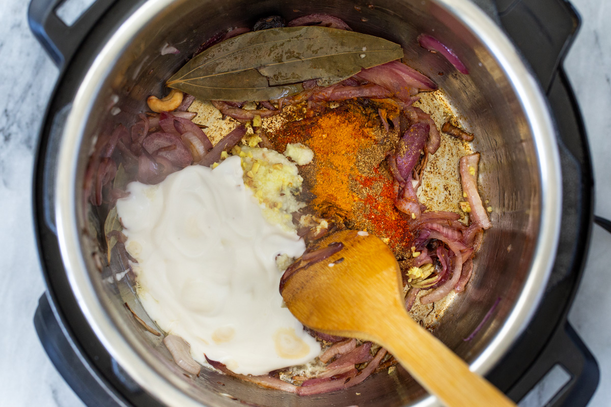 ground spices and yogurt being added to an Instant Pot with sauteed onion