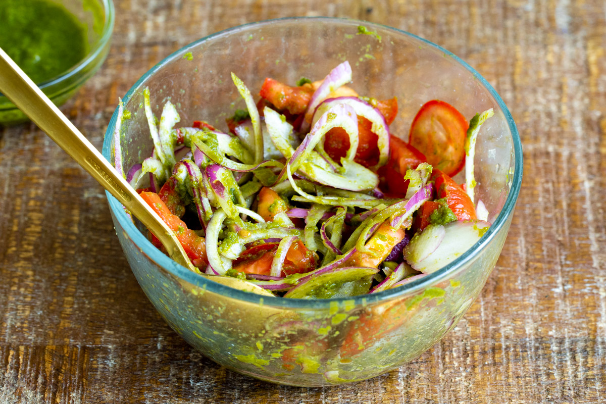 onion, tomatoes and cilantro mint chutney being mixed in a glass bowl