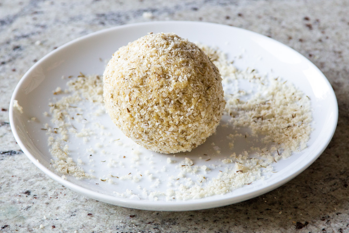 vegan cheese ball being coated breadcrumbs and seasonings