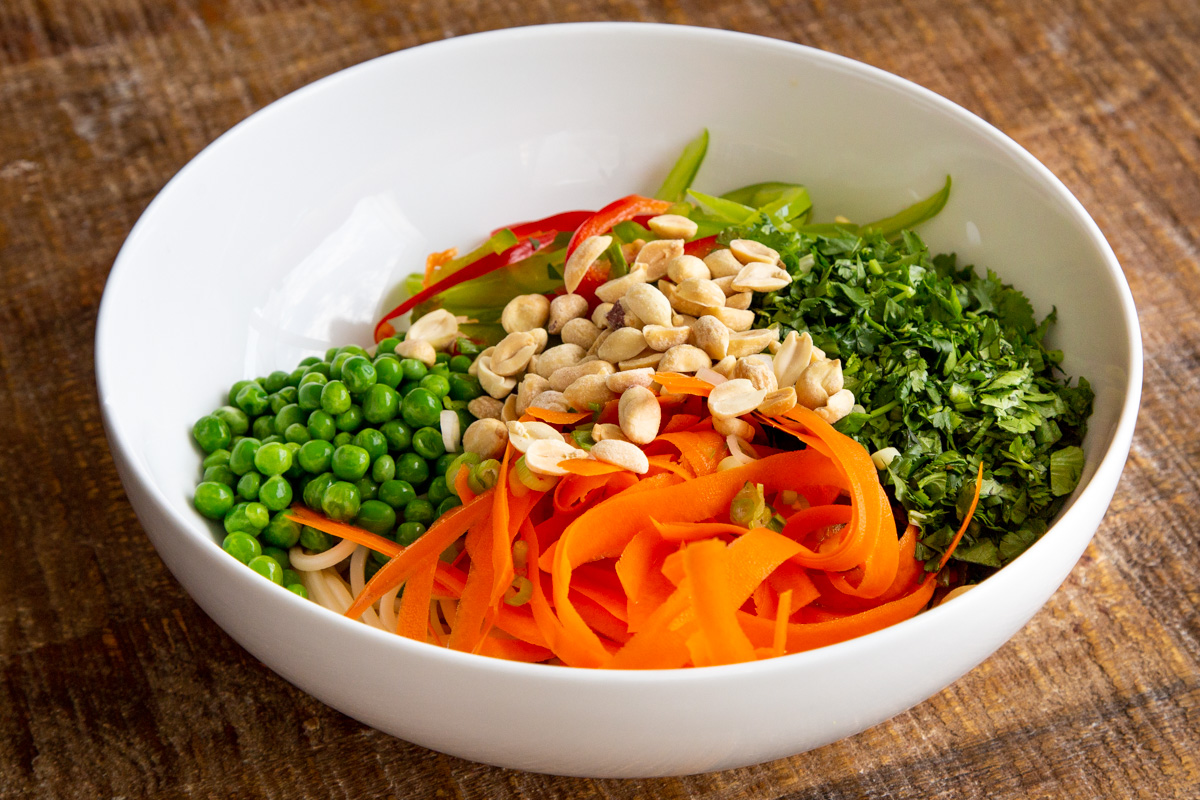 veggies and cooked spaghetti in a white bowl sprinkled with peanuts
