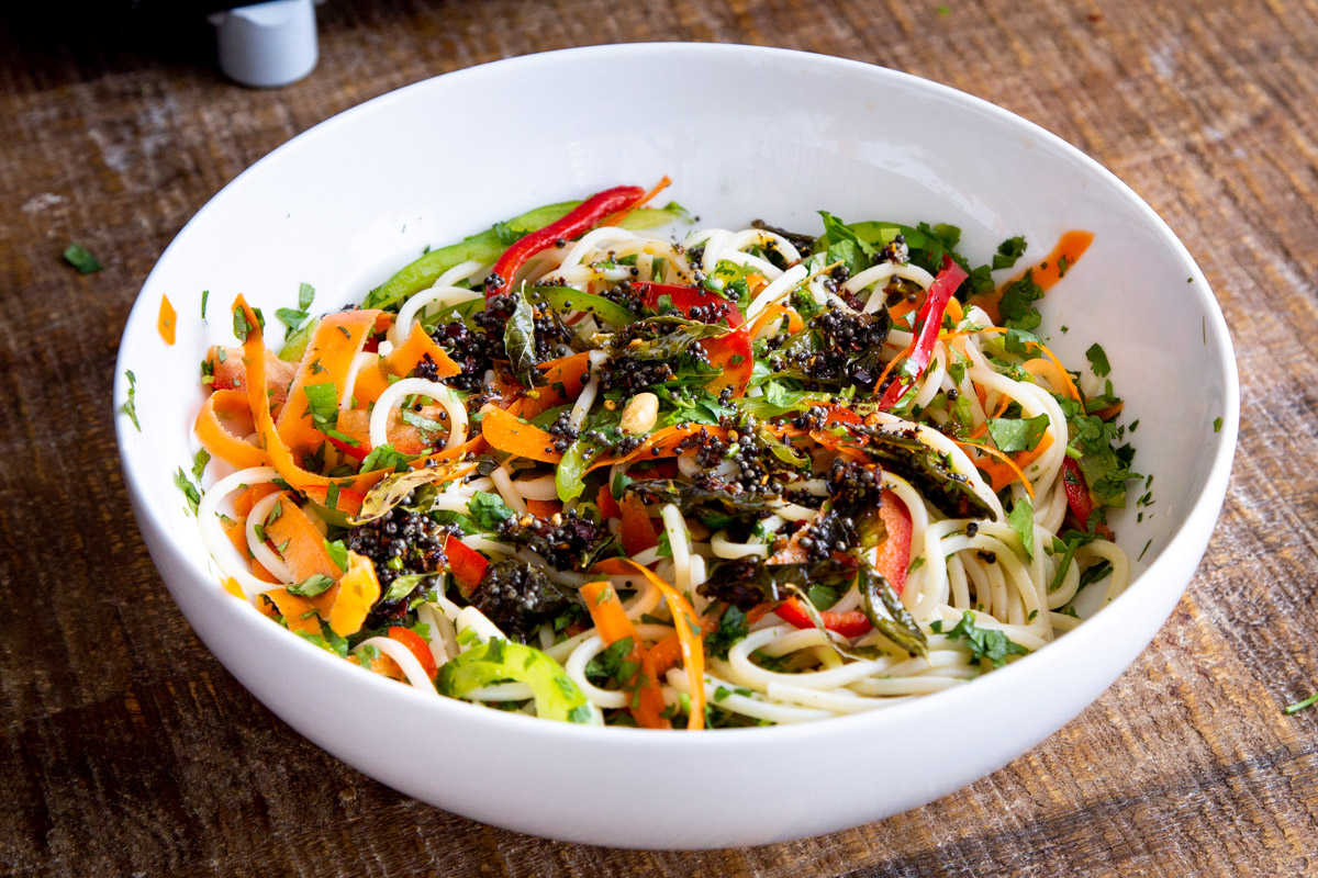 pasta salad, and veggies with tadka tempering being mixed in a white salad bowl