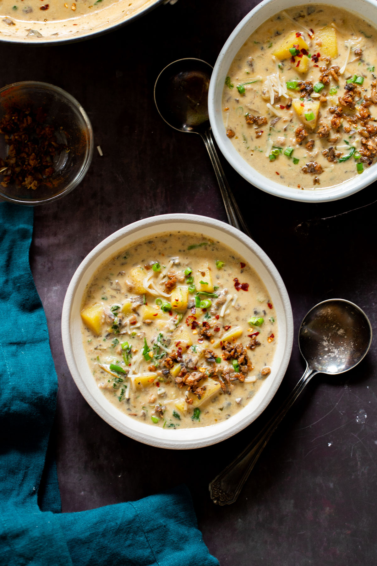 two bowls of vegan zuppa toscana with two silver spoons on the side